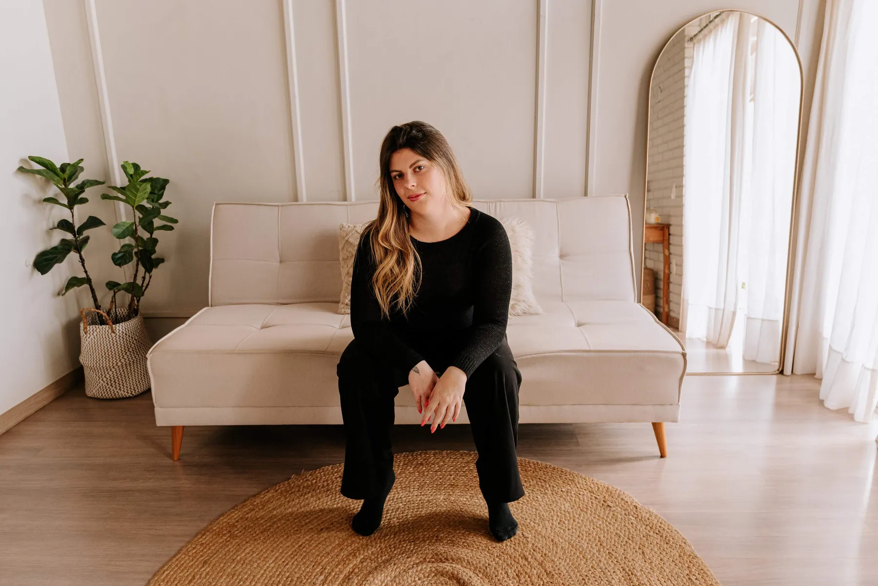 Adriana, fundadora da ArteNova, sentada em um sofá claro, olhando para a câmera